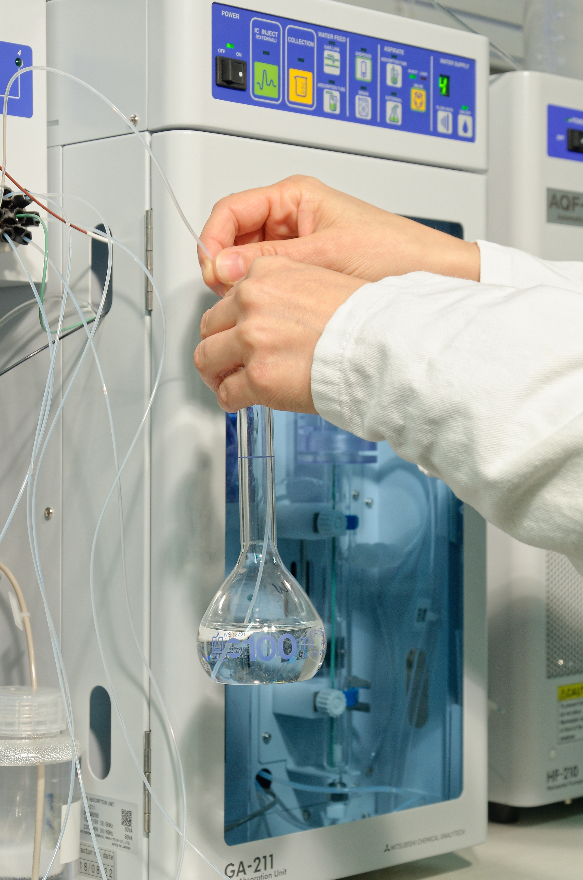 2 hands are holding a vial in front of laboratory equipment